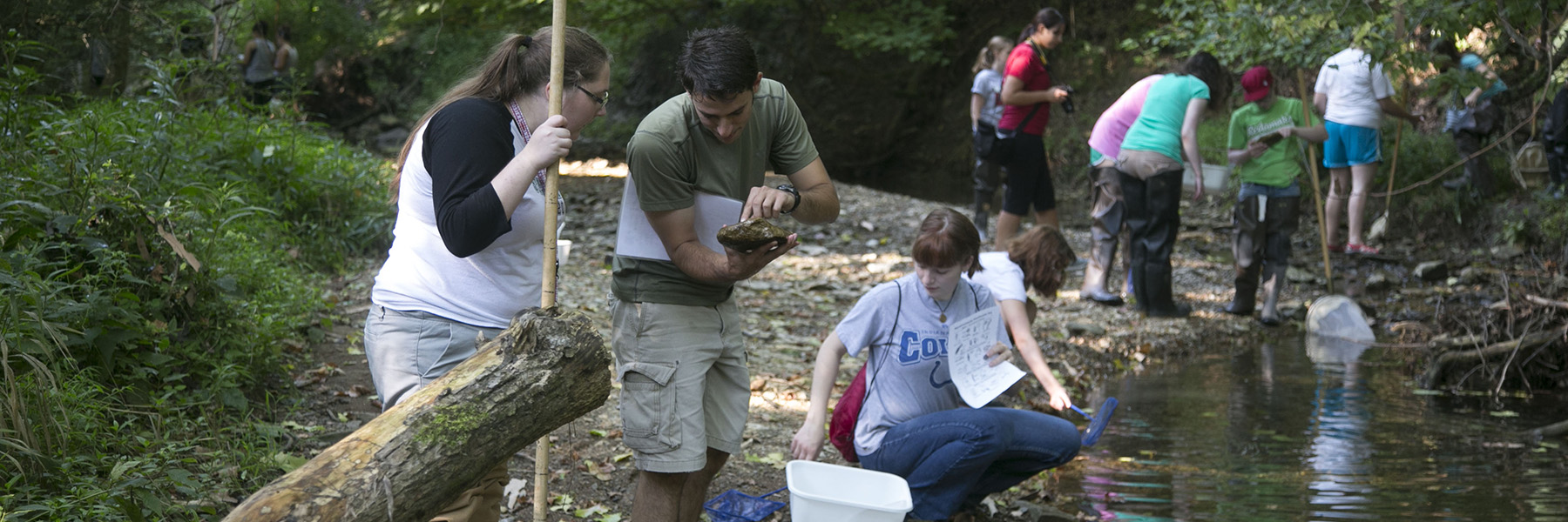 Two Citizen Scientists look under a rock for macroinvertebrates.
